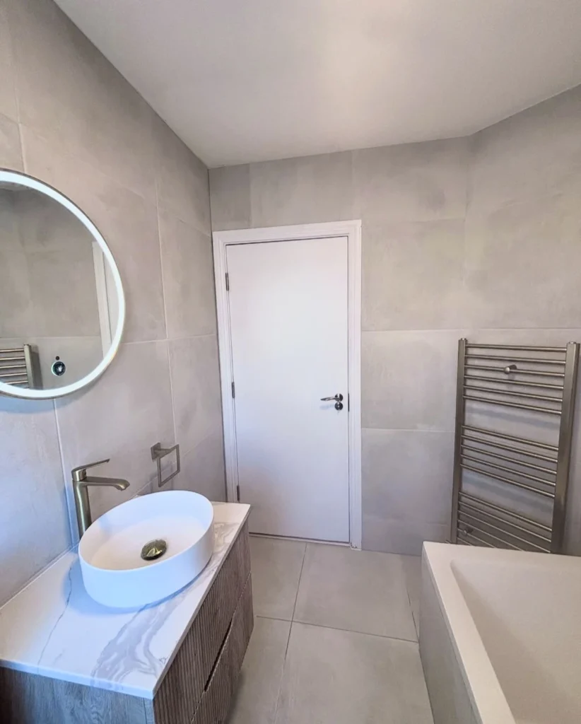 Lyse fliser og glasvægge der reflekterer lyset på badeværelset