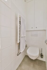 Lille badeværelse med væghængt toilet, hvide fliser og indbygget skab