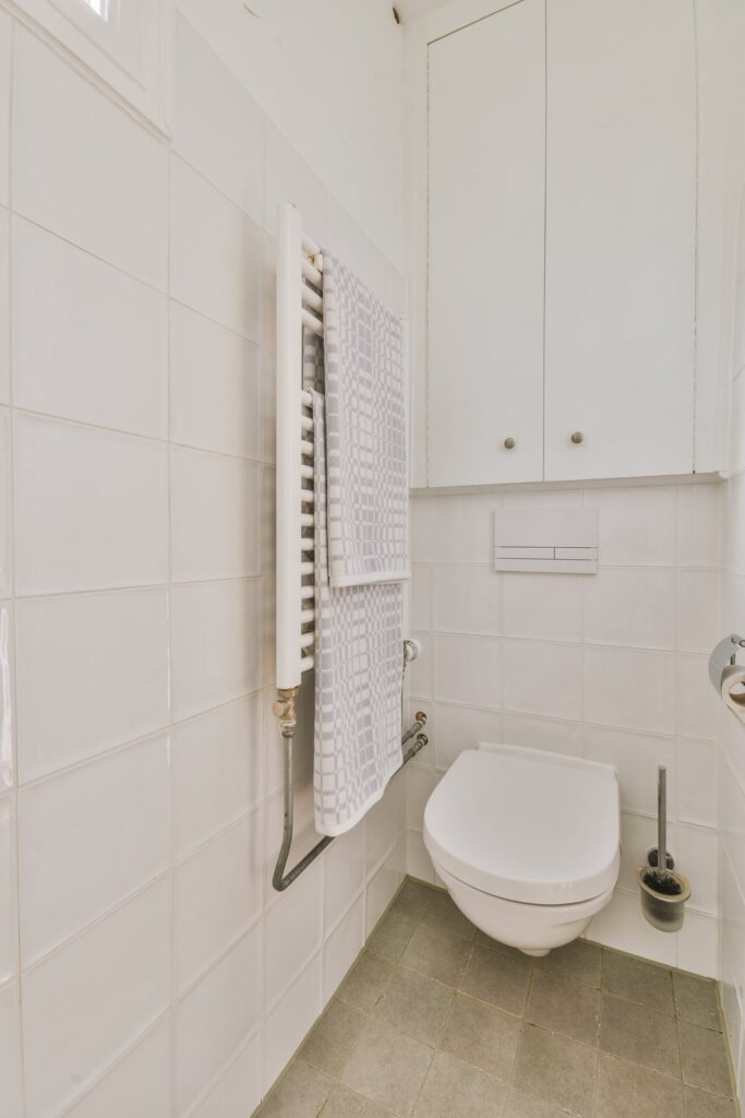 Lille badeværelse med væghængt toilet, hvide fliser og indbygget skab